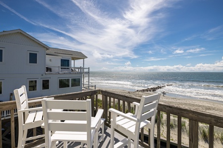 The beachfront property sits directly on sandy shores with stunning ocean views. Your private deck features seating where you can watch surfers ride the waves just steps from your door.