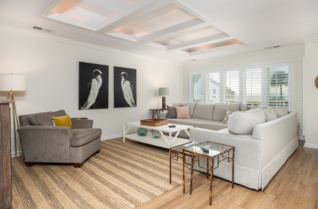 Sink into plush gray seating while enjoying natural light from plantation shutters and the elegant coffered ceiling above.