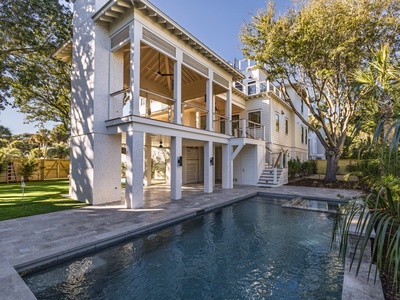 Modern two-story vacation home featuring contemporary architecture with palm trees and pool area in the front yard.