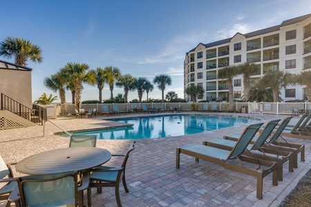 Large community pool with lounge seating and palm-lined surroundings