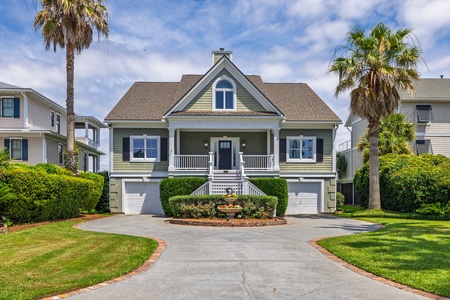 This charming coastal property features classic architecture with a welcoming front porch, nestled among swaying palms and manicured landscaping, offering an inviting arrival experience.