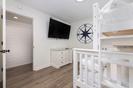 Your bright bunk room features coastal charm with a compass wall accent, flat-screen TV, and nautical touches for a cozy stay.