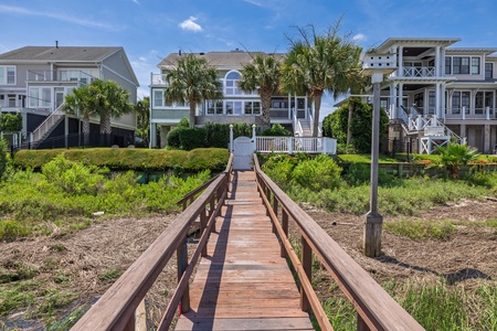 This waterfront property features a private dock and boardwalk leading directly to the main residence, surrounded by coastal palm trees and neighboring beach homes in a quiet residential area.