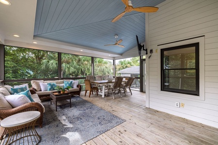 Spacious screened porch with ceiling fan, outdoor dining table, and comfortable seating — ideal for evening meals in the coastal breeze