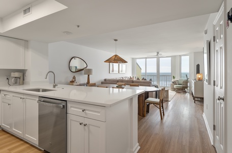 Your open-concept retreat features a sleek kitchen island flowing into coastal living space with breathtaking ocean views through floor-to-ceiling windows.