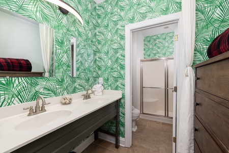 Fresh up in your vibrant tropical bathroom featuring dual vanities and bold palm wallpaper that brings vacation vibes to your daily routine.