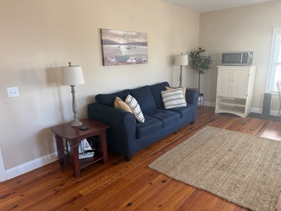 Relax in your cozy living room with plush navy sofa, warm hardwood floors, and modern amenities like microwave and entertainment center.