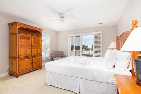 Relax in your spacious bedroom featuring plush linens, wooden furnishings, and balcony doors that frame serene coastal views. Wake to natural light and gentle sea breezes.