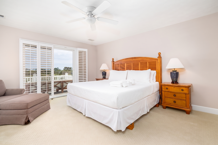 Sink into crisp white linens and wake to peaceful views through shuttered doors. Your ceiling fan keeps the breeze going while warm wood tones and cozy seating invite total relaxation.