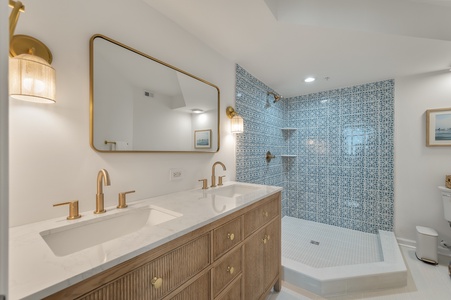 Step into your luxurious en-suite bathroom featuring dual vanities, brass fixtures, and a stunning geometric-tiled shower for ultimate relaxation.