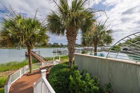 Waterfront property featuring a private wooden dock, palm-lined deck, and scenic views across the marina with boat slips and neighboring docks.