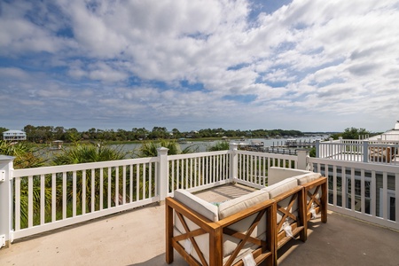Private balcony overlooks calm waterfront marina and lush coastal scenery, offering serene views and outdoor seating for relaxation.