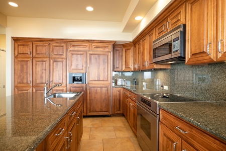 Fully stocked gourmet kitchen with rich wood cabinetry, granite counters, and high-end stainless appliances.