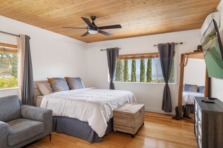The spacious primary suite features a king-size bed, warm wood ceilings, ensuite bath access, and views of Makakilo’s rolling hills.