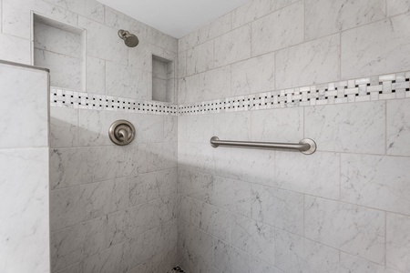 Walk-in shower with tiled walls and convenient grab bars.