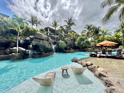 This resort-style pool features waterfalls, lounge chairs in the water, and a serene tropical setting perfect for relaxation.