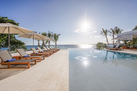 Lounge by the infinity pool overlooking the ocean, with plenty of sunbeds and umbrellas.