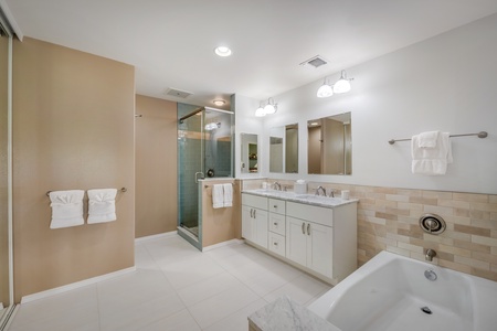 Spacious ensuite primary bath with dual sinks, a large soaking tub, and a glass-enclosed shower.
