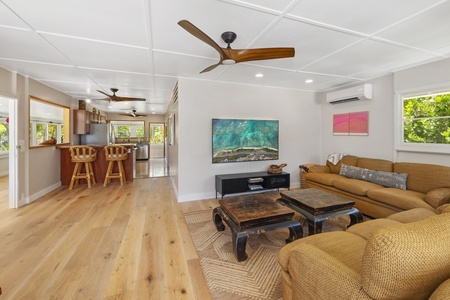 The living area features plush sectionals, a large TV, split AC, and an open layout that flows seamlessly into the kitchen.