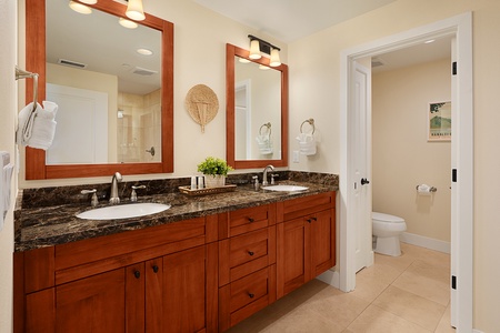 Your private bathroom features dual vanities with granite countertops, warm wood cabinetry, and fresh towels waiting for your arrival.