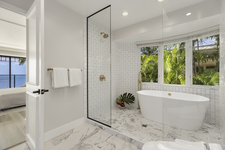 Spa-style guest bath with soaking tub and walk-in shower surrounded by tropical views.