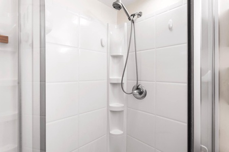Step into your pristine white-tiled shower with modern fixtures and built-in corner shelving for your essentials.
