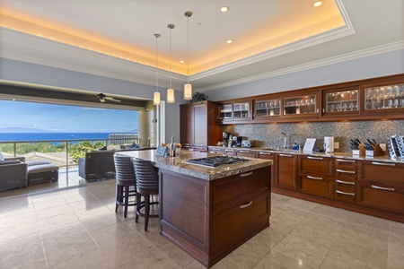 The gourmet kitchen is a chef's dream, featuring a large central island with seating, top-of-the-line appliances, and rich wood cabinetry. The open design allows you to enjoy stunning ocean views while preparing meals, with elegant pendant lighting.