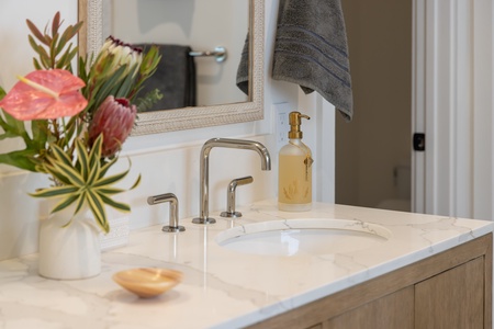Elegant details like brushed gold fixtures, fresh florals, and a quartz vanity elevate the bath to a spa-like retreat.