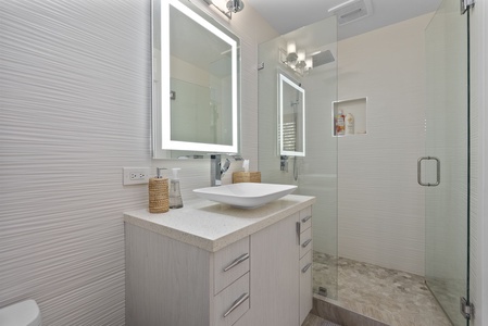 Modern ensuite bath with glass shower and illuminated mirror.