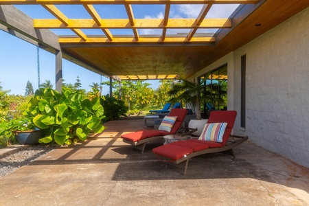 Lounge chairs under the pergola, surrounded by tropical landscaping.