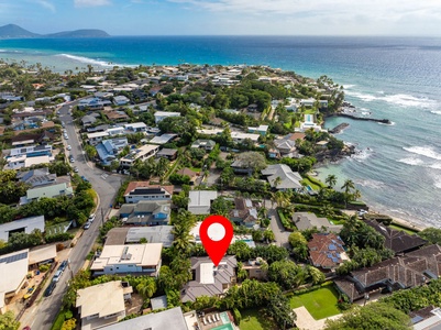 Aerial view of neighborhood with the property marked by red pin near pristine coastline and tropical surroundings.