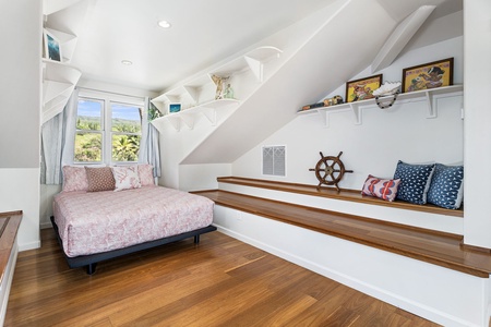 Your cozy attic retreat features built-in seating, charming nautical touches, and warm wood floors beneath vaulted ceilings.