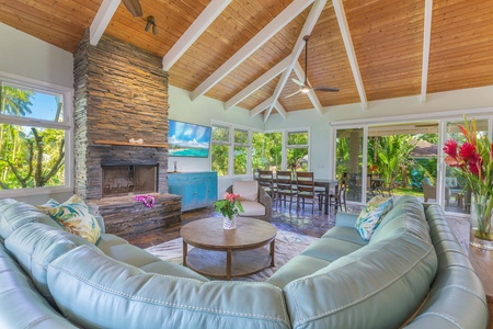 Pohaku Villa’s open-concept living room blends vaulted wood ceilings, a stone-accent fireplace, and seamless indoor-outdoor flow.