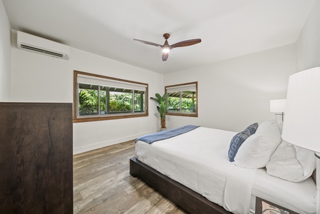 Primary bedroom with king bed, ceiling fan, and peaceful garden views from large windows.