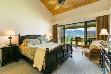 Spacious bedroom with a king-sized bed, elegant furnishings, and access to a private lanai offering breathtaking mountain views.