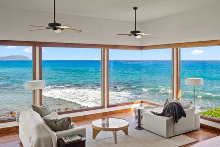 Relax in this stunning oceanfront living room with soaring beamed ceilings, stone fireplace, and breathtaking sea views from every window.