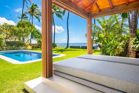 Ocean-view daybed tucked beneath a shaded pavilion—perfect for reading, napping, or coastal cocktails.