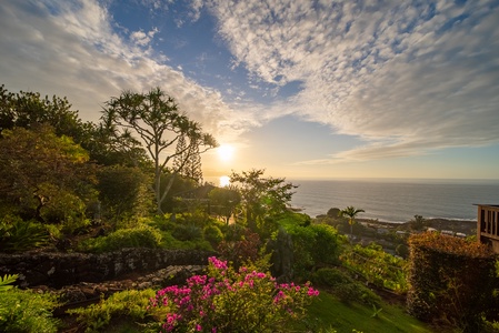 Stunning coastal sunset illuminates lush tropical gardens overlooking the ocean, creating a breathtaking natural backdrop for the property.
