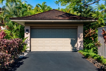 Garage and driveway framed by lush green landscaping.