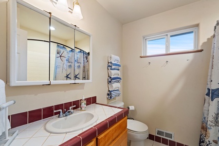 Your private bathroom features nautical-themed touches with colorful tile accents, fluffy towels, and natural light from the window.