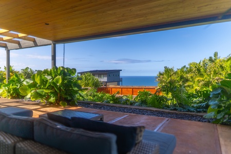 Cozy seating area under a shaded lanai with stunning ocean views in the background.