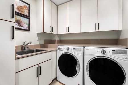 Laundry room with full-size washer, dryer, sink, and storage space.