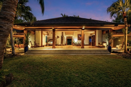 Tropical villa exterior showcasing open-air design with warm lighting and lush palm trees in the evening twilight.
