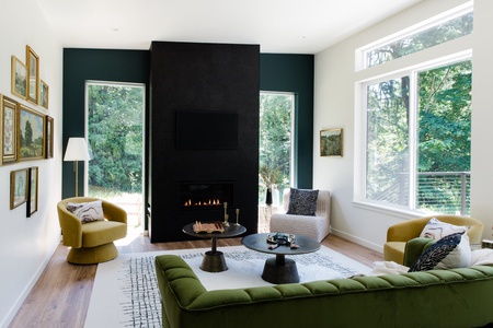 Relax in the light-filled living room, where soaring windows frame peaceful forest views and a modern fireplace creates a warm gathering space after a day of Pacific Northwest adventures.