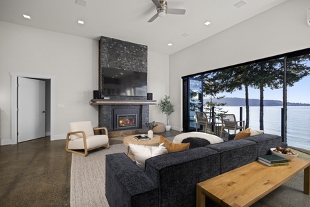 Inviting living room with cozy fireplace and full wall of glass showcasing sweeping views of Bellingham Bay.