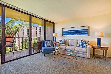 This cozy living room invites you to relax and unwind, featuring comfortable seating with a tropical view through the large sliding glass doors