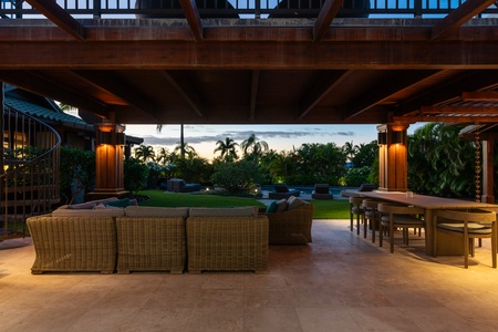 Covered lanai at dusk with cozy seating and a dining area, offering a tranquil space.