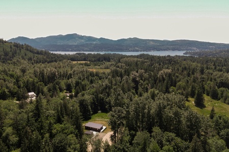 Aerial view of the property nestled in a forested setting with lake and mountain scenery in the surrounding area.