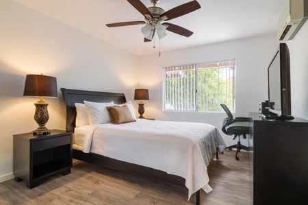Unwind in your comfortable bedroom featuring a plush bed, workspace, and ceiling fan for the perfect night's rest.