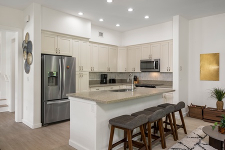 The bright kitchen features many amenities including a fridge, oven, extended counter-tops and bright lighting.